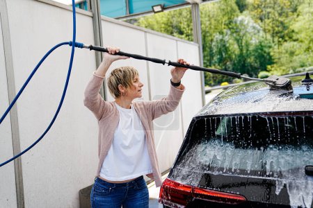 Téléchargez les photos : Atteignant haut, une femme utilise une brosse savonneuse sur le toit de sa voiture. - en image libre de droit
