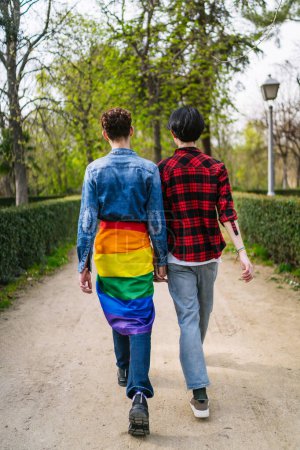 A joyful gay couple, Latino with an LGBT flag, strolling in a lush park.