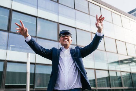 Un entrepreneur en costume s'engage joyeusement avec des lunettes de réalité virtuelle tout en se tenant devant un élégant immeuble de bureaux vitré.
