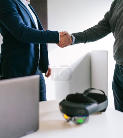 Vue rapprochée d'une poignée de main entre un homme d'affaires et un client, symbolisant l'accord réussi pour les lunettes VR dans un bureau.