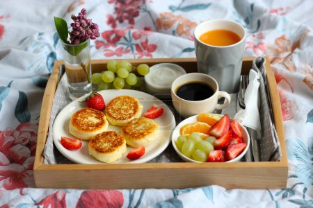 Breakfast in bed - cottage cheese cheesecakes with black coffee, orange juice, sour cream and fresh fruits