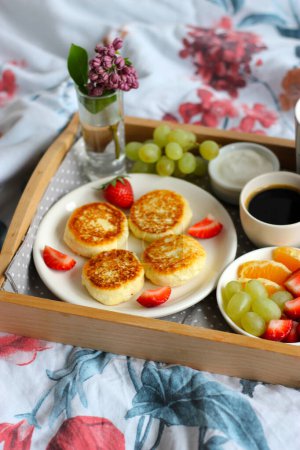 Breakfast in bed - cottage cheese cheesecakes with black coffee, orange juice, sour cream and fresh fruits