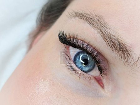 Nahaufnahme des geöffneten blauen Auges mit Wimpernverlängerungen im Schönheitssalon Makroansicht. 