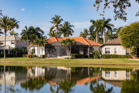 A beautiful summer house in South Florida on a sunny day. Typical concrete house on the shore of a lake in southwest Florida in the countryside with palm trees, tropical plants and flowers, lawn and pine trees. Florida.