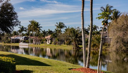 Una hermosa casa de verano en el sur de Florida en un día soleado. Casa típica de hormigón en la orilla de un lago en el suroeste de Florida en el campo con palmeras, plantas tropicales y flores, césped y pinos. Florida.