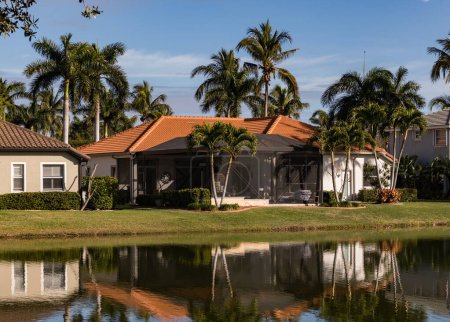 A beautiful summer house in South Florida on a sunny day. Typical concrete house on the shore of a lake in southwest Florida in the countryside with palm trees, tropical plants and flowers, lawn and pine trees. Florida.