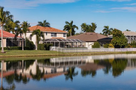 Ein schönes Sommerhaus in Südflorida an einem sonnigen Tag. Typisches Betonhaus am Ufer eines Sees im Südwesten Floridas auf dem Land mit Palmen, tropischen Pflanzen und Blumen, Rasen und Kiefern. Florida.