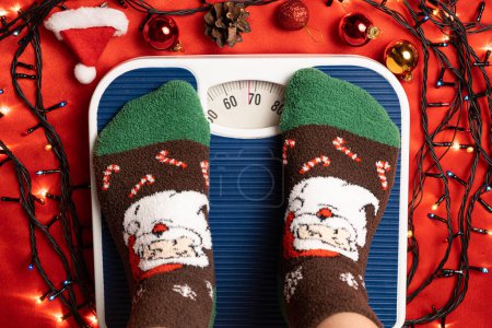 A woman in Christmas socks stands on the scales, weighs herself after gluttony during the holidays.