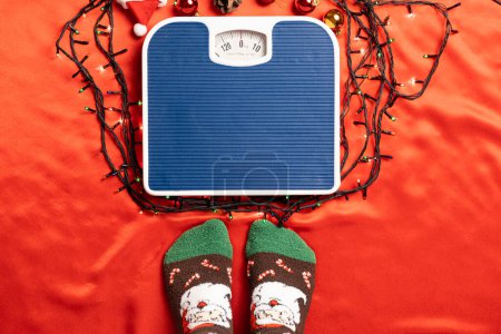 Foto de Una mujer va a pararse en la balanza sobre un fondo rojo, peso después de las vacaciones de Navidad. - Imagen libre de derechos