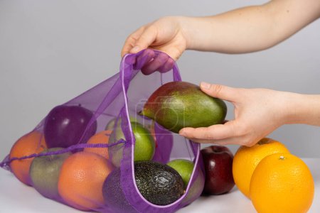 Téléchargez les photos : Une femme met des fruits dans un filet. Le concept d'abandon des sacs à provisions en plastique. - en image libre de droit