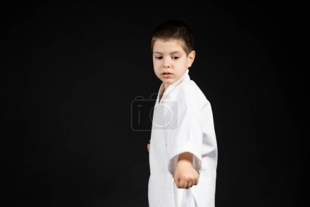 Photo for A little boy practices martial arts, karate classes in kimono on a black background, a place for text. - Royalty Free Image