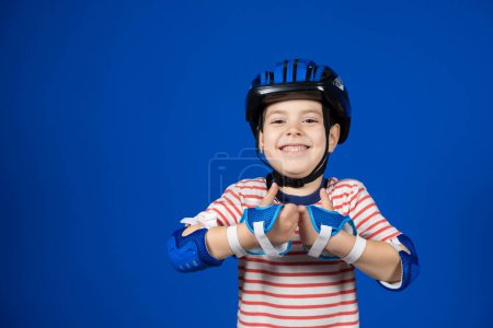 Photo for A boy in a helmet and gloves shows thumbs up on a blue background. - Royalty Free Image