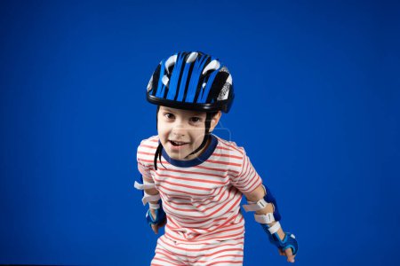 Photo for A happy boy in a protective helmet, elbow pads and gloves on a blue background. Protection when riding a bicycle, skateboard, roller skate. - Royalty Free Image