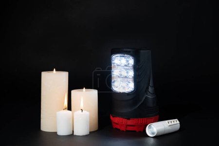 Linternas eléctricas y velas encendidas sobre fondo negro, fuentes alternativas de luz y calor.