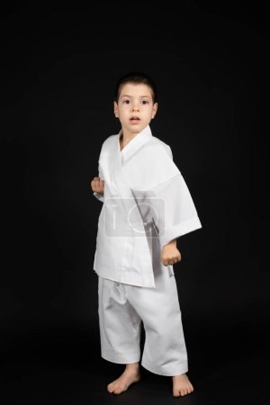 Photo for A little boy practices martial arts, karate classes in kimono on a black background. - Royalty Free Image
