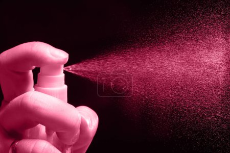 Photo for Man sprinkles a spray of perfume on a black background. Color of the year 2023 Viva Magenta. - Royalty Free Image