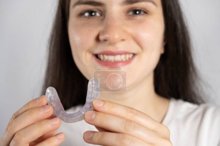 Téléchargez les photos : Une femme tient un protège-dents dentaire, une attelle pour le traitement du dysfonctionnement des articulations temporomandibulaires, du bruxisme, de la malocclusion, pour détendre les muscles de la mâchoire - en image libre de droit