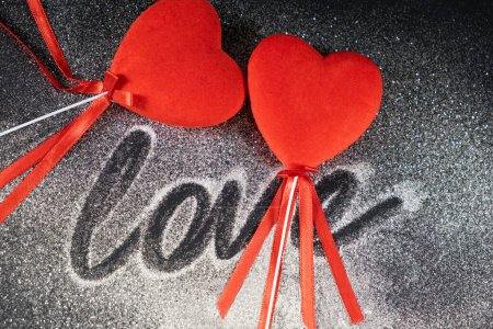 Foto de Día de San Valentín, dos corazones rojos amorosos sobre un fondo negro con lentejuelas y el texto del amor - Imagen libre de derechos