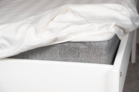 Foto de Hoja de satén blanco en una banda elástica en el colchón. Ropa de cama en la cama. - Imagen libre de derechos