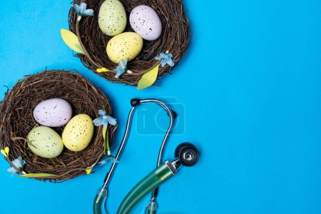 Ostermedizin. Zwei Nester mit bemalten Eiern und einem Stethoskop auf blauem Hintergrund, Platz für Text.