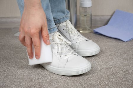 Foto de Una mujer limpia las zapatillas de deporte de polvo y suciedad con una esponja de melamina. - Imagen libre de derechos