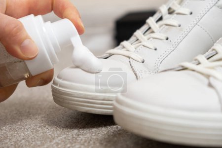 Téléchargez les photos : Appliquer de la mousse nettoyante de la bouteille sur des baskets en cuir blanc pour femmes. Entretien pour chaussures en cuir, blanchiment de surface. - en image libre de droit