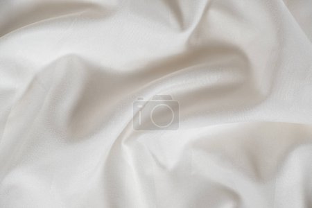 Foto de Satin crumpled fabric of light milky color, top view. Natural bed linen, sheets, abstract background of luxury fabric, wavy folds. - Imagen libre de derechos