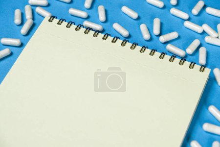 Notatnik medyczny z tabletkami na niebieskim tle, miejsce na tekst.