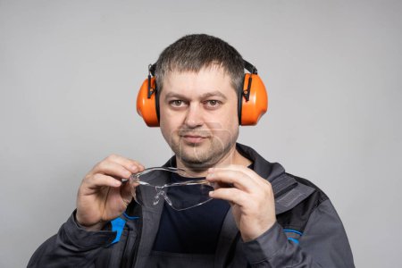 Téléchargez les photos : Un constructeur portant des protecteurs d'oreille porte des lunettes sur un fond blanc. - en image libre de droit
