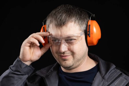 Téléchargez les photos : Un homme en cache-oreilles, lunettes et salopettes sur fond noir - en image libre de droit