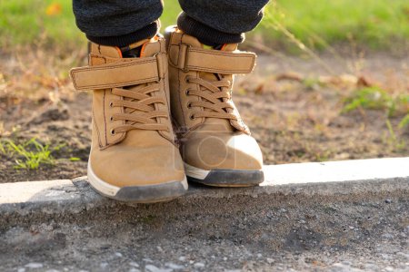 Téléchargez les photos : Pieds d'un petit garçon en nubuck marron à l'automne dans un parc de la ville. Chaussures semi-saison imperméables confortables. - en image libre de droit