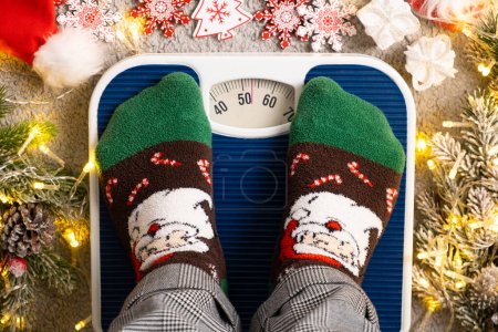 A woman in Christmas socks stands on the scales, weighs herself after gluttony during the holidays.
