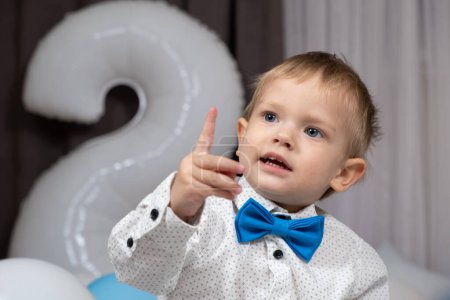 Téléchargez les photos : Portrait de mignon garçon de deux ans montrant index vers le haut - en image libre de droit