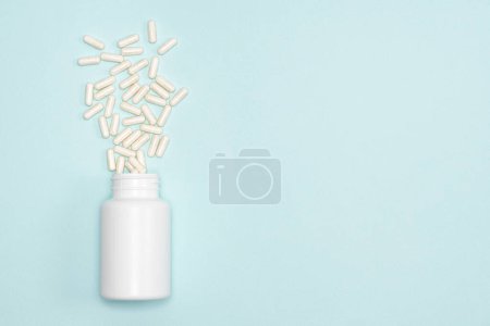 Photo for Medical jar with scattered white capsules on blue background with space for text - Royalty Free Image