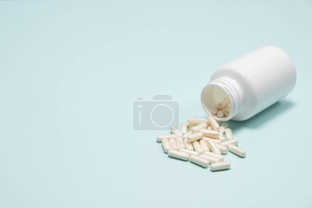Photo for Medical jar with scattered white capsules on blue background with space for text - Royalty Free Image