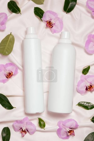 Liquid laundry detergent and fabric softener on bedding, orchid flowers, top view.