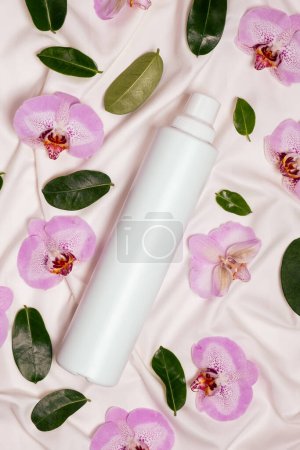 Fabric softener with floral scent among flowers on bed linen top view