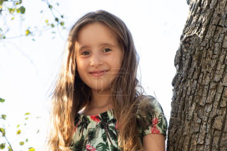 Téléchargez les photos : Jolie fille de cinq ans assise sur un arbre en été dans la nature. - en image libre de droit