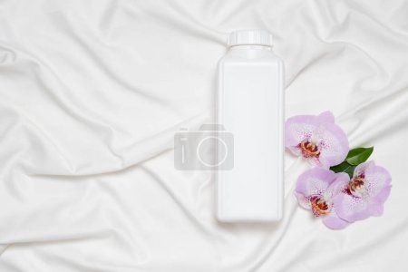 Liquid laundry detergent or fabric softener on bedding, orchid flowers, top view.