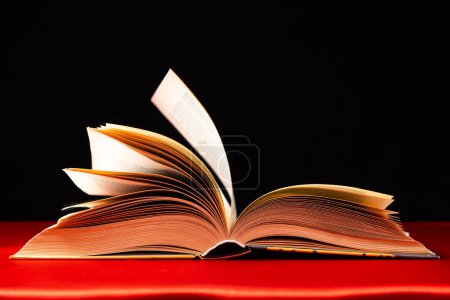 Les pages d'un livre épais sont tournées sur un fond rouge et noir
