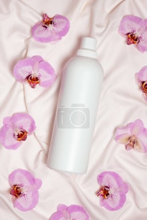 Washing liquid or fabric softener on bed linen with orchid flowers, top view.