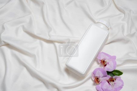 Waschmittel oder Weichspüler auf Bettwäsche mit Orchideenblüten, Ansicht von oben.