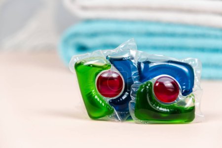 Laundry pods capsules on beige background with soft towels.