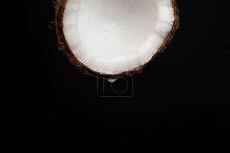 Photo for A drop of coconut water dripping from half a coconut on a black background, space for text. - Royalty Free Image