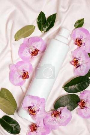 Ecological laundry detergent among orchid flowers on bed linen top view