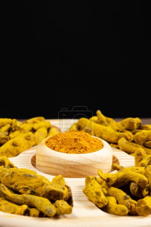 Téléchargez les photos : Poudre de curcuma et racine de curcuma séchée sur plateau en bois sur fond noir - en image libre de droit