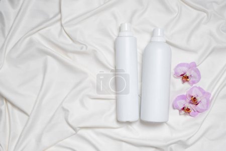 Liquid laundry detergent and fabric softener on bedding, orchid flowers, space for text.