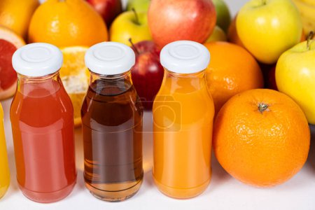 Foto de Surtido de zumos de frutas en frascos de vidrio entre frutas sobre fondo blanco. - Imagen libre de derechos