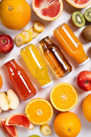 Foto de Surtido de zumos de frutas en frascos de vidrio entre frutas sobre fondo blanco vista superior. - Imagen libre de derechos