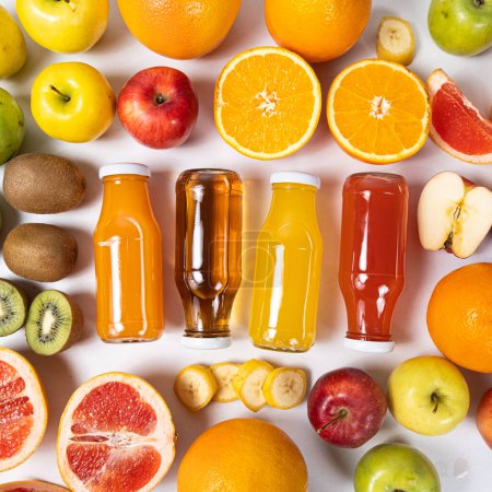 Foto de Surtido de zumos de frutas en frascos de vidrio entre frutas sobre fondo blanco vista superior. - Imagen libre de derechos